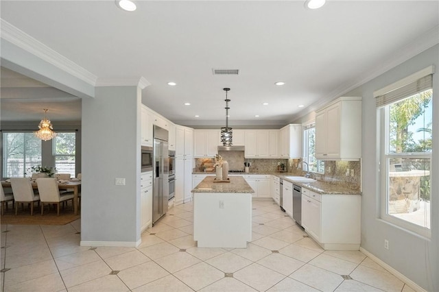 24274 Reyes Adobe Way, Valencia, CA 91354 - kitchen featuring appliances with stainless steel finishes, backsplash, light stone countertops, a center island, and crown molding