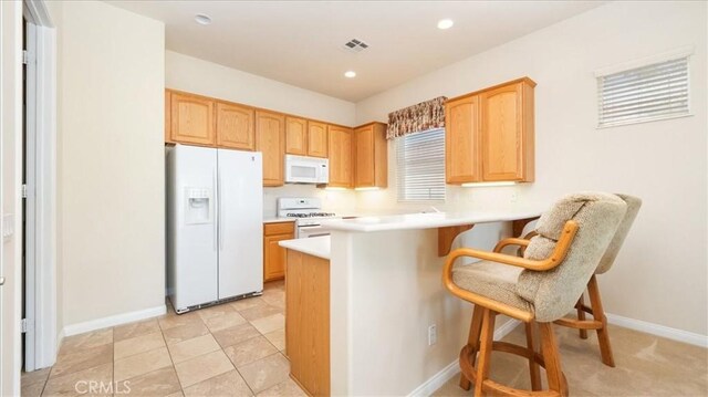 19484 Vermillion Ln, Apple Valley, CA 92308 - kitchen with white appliances, a kitchen breakfast bar, a peninsula, light brown cabinets, and light countertops