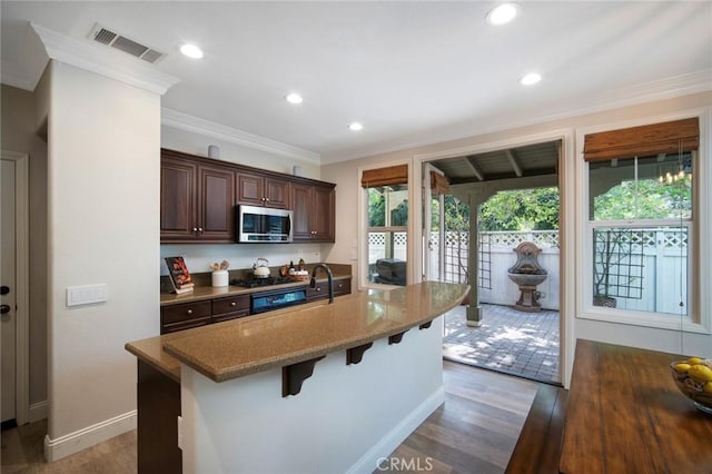 1 Evergreen Rd, Ladera Ranch, CA 92694 - kitchen featuring stainless steel microwave, a breakfast bar, a kitchen island with sink, wood finished floors, and ornamental molding