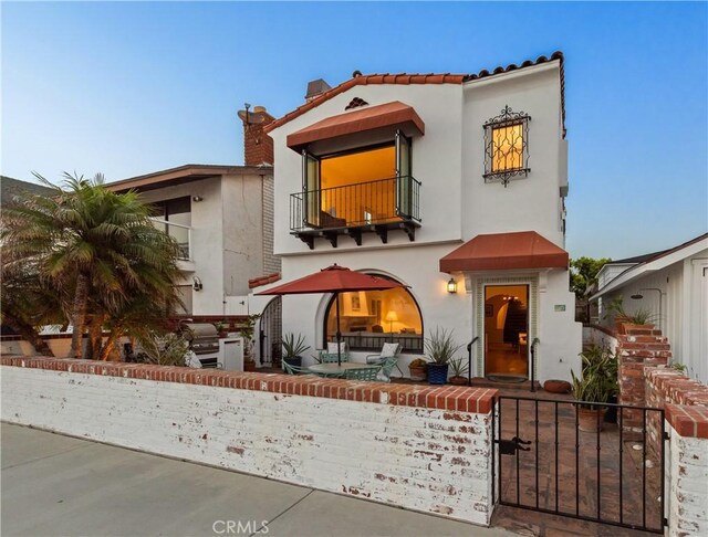 1305 E Balboa Blvd, Newport Beach, CA 92661 - mediterranean / spanish home with a balcony, a fenced front yard, stucco siding, a gate, and a chimney