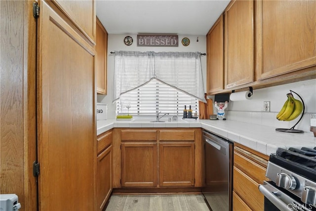 140 W 220th St Unit 105, Carson, CA 90745 - kitchen with appliances with stainless steel finishes, a sink, light wood-style floors, tile countertops, and brown cabinets