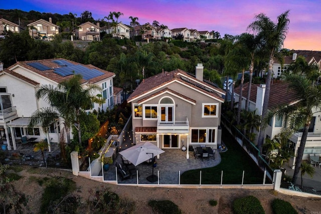 9552 Babauta Rd, San Diego, CA 92129 - back of property at dusk featuring a balcony, a patio, a residential view, a fenced backyard, and a chimney