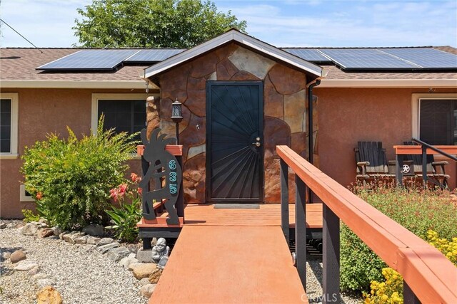 635 5th St, Willows, CA 95988 - doorway to property with roof mounted solar panels, stucco siding, and roof with shingles