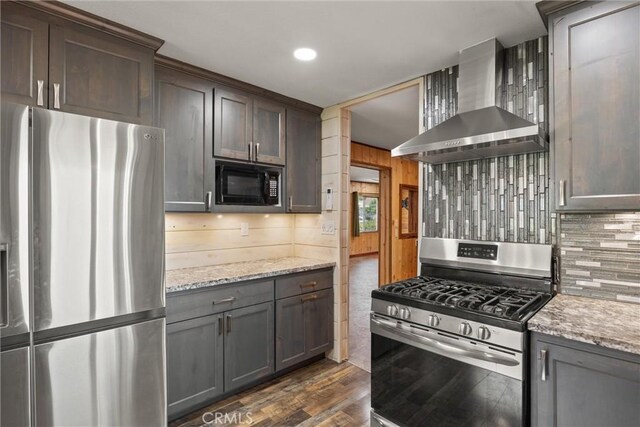 635 5th St, Willows, CA 95988 - kitchen featuring appliances with stainless steel finishes, wall chimney range hood, decorative backsplash, dark wood finished floors, and light stone counters