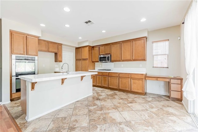 37245 La Lune Ave, Murrieta, CA 92563 - kitchen featuring stainless steel appliances, brown cabinets, a center island with sink, recessed lighting, and a sink