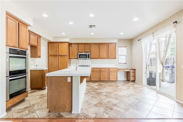 37245 La Lune Ave, Murrieta, CA 92563 - kitchen featuring stainless steel appliances, tile countertops, brown cabinets, a kitchen island with sink, and recessed lighting