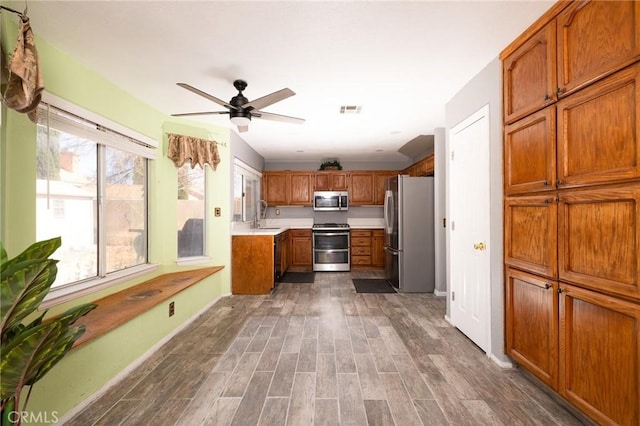 12609 Gentle Breeze Way, Victorville, CA 92392 - kitchen with appliances with stainless steel finishes, brown cabinetry, light countertops, ceiling fan, and wood finished floors