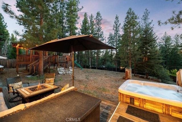 114 Starvation Flats Rd, Big Bear Lake, CA 92315 - yard at dusk with a hot tub, a playground, an outdoor fire pit, a wooden deck, and a fenced backyard
