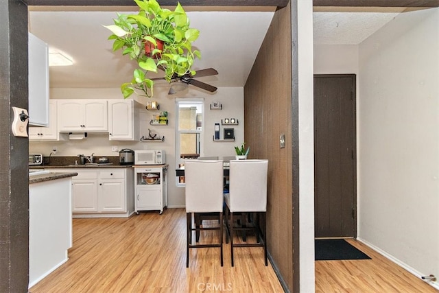 1000 W Macarthur Blvd Unit 44, Santa Ana, CA 92707 - kitchen featuring white microwave, light wood-type flooring, dark countertops, a sink, and white cabinetry