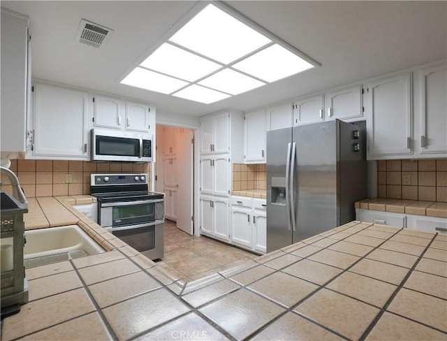 5030 Cardiff Ln, Atwater, CA 95301 - kitchen with stainless steel appliances, tile counters, decorative backsplash, and white cabinetry