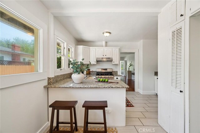 1241 Bresee Ave, Pasadena, CA 91104 - kitchen with gas range, under cabinet range hood, a peninsula, white cabinets, and light stone counters