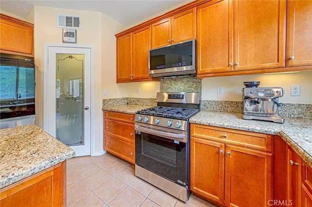 25238 Gloriso Ln, Stevenson Ranch, CA 91381 - kitchen with stainless steel appliances, light tile patterned floors, brown cabinets, light stone counters, and a sink