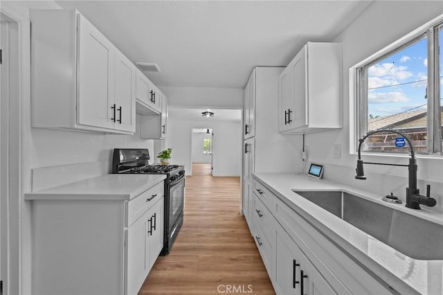 24576 4th St, San Bernardino, CA 92410 - kitchen with black gas stove, a sink, light countertops, light wood-style floors, and white cabinetry