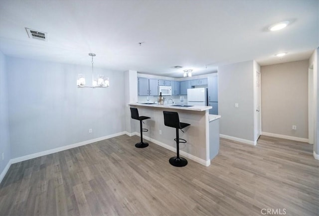 31241 Taylor Ln, Temecula, CA 92592 - kitchen featuring white appliances, a peninsula, light wood-style flooring, a kitchen bar, and light countertops