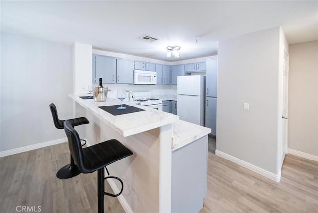 31241 Taylor Ln, Temecula, CA 92592 - kitchen featuring white appliances, a peninsula, a kitchen breakfast bar, light countertops, and light wood-type flooring