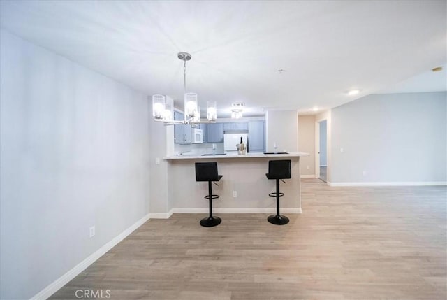 31241 Taylor Ln, Temecula, CA 92592 - kitchen featuring light wood finished floors, a kitchen bar, refrigerator, a chandelier, and light countertops