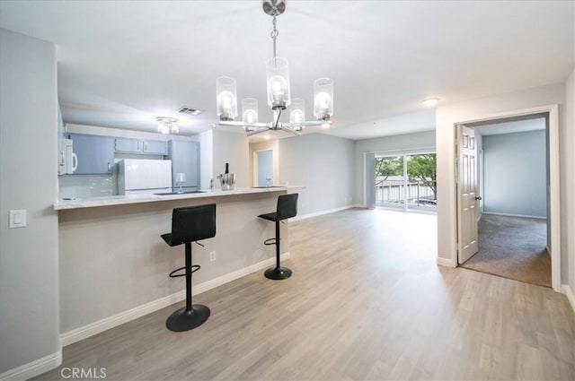 31241 Taylor Ln, Temecula, CA 92592 - kitchen with fridge, white microwave, light wood-style flooring, baseboards, and a breakfast bar area