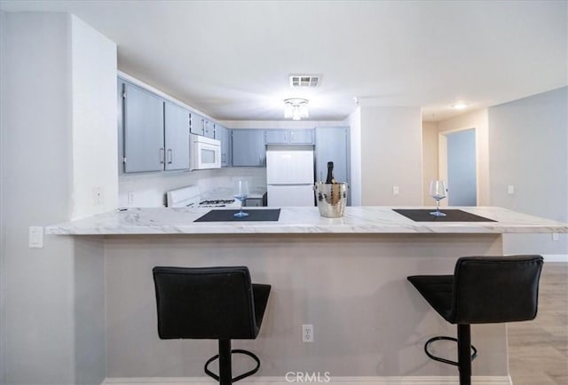 31241 Taylor Ln, Temecula, CA 92592 - kitchen featuring white appliances, a peninsula, a breakfast bar, baseboards, and light wood-style floors