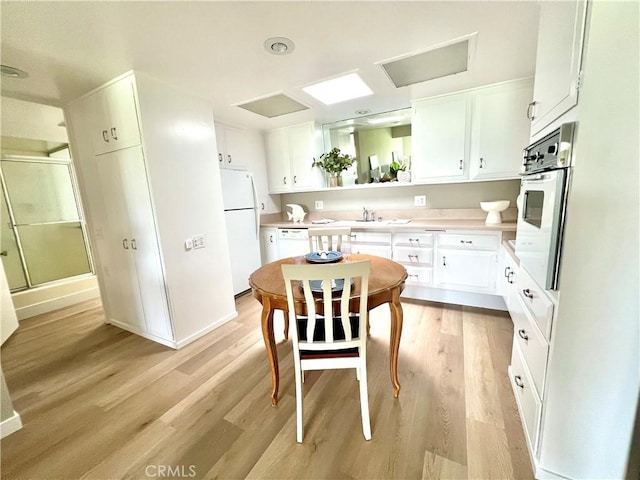 13580 Medinac Ln Unit M5-E, Seal Beach, CA 90740 - kitchen with white appliances, white cabinets, light wood finished floors, light countertops, and baseboards