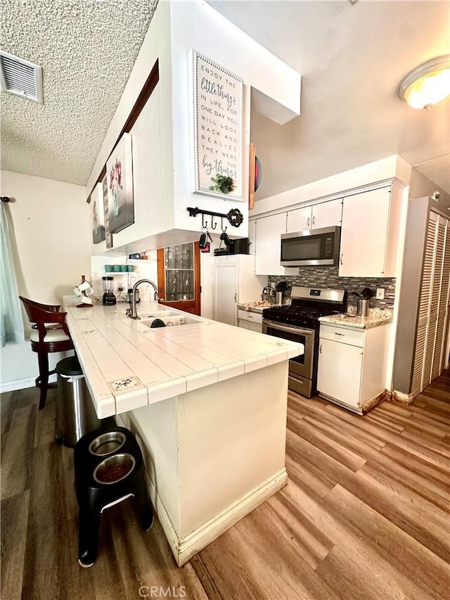 3346 Sunnyside Dr, Riverside, CA 92506 - kitchen featuring appliances with stainless steel finishes, a peninsula, a sink, tile counters, and light wood-style floors
