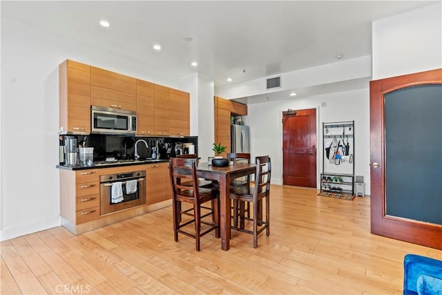 460 S Spring St Unit 613, Los Angeles, CA 90013 - kitchen featuring appliances with stainless steel finishes, light wood finished floors, dark countertops, recessed lighting, and backsplash