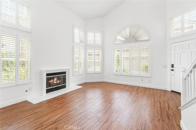 24545 Santa Clara Ave, Dana Point, CA 92629 - unfurnished living room with high vaulted ceiling, a glass covered fireplace, wood finished floors, plenty of natural light, and stairs
