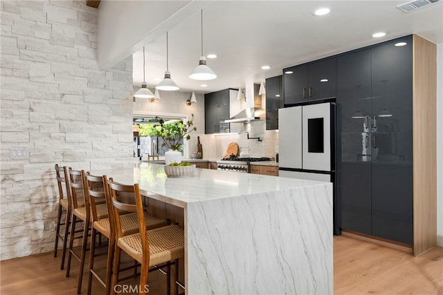 19851 Malaga Ln, Yorba Linda, CA 92886 - kitchen featuring wall chimney range hood, freestanding refrigerator, light wood-style floors, dark cabinetry, and a breakfast bar area