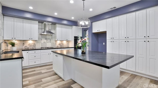 2431 Elizabeth Ct, Upland, CA 91784 - kitchen with wall chimney exhaust hood, dark countertops, stainless steel gas cooktop, light wood-style floors, and decorative backsplash