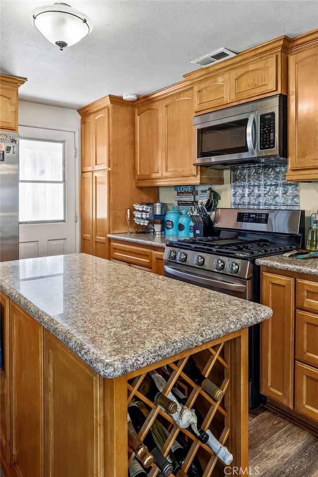 5644 Wadsworth Ave, Highland, CA 92346 - kitchen with appliances with stainless steel finishes, a textured ceiling, a center island, dark wood-style floors, and brown cabinetry