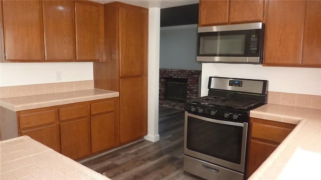 284 Celeste Dr, Riverside, CA 92507 - kitchen with appliances with stainless steel finishes, dark wood-style floors, tile countertops, brown cabinets, and a brick fireplace