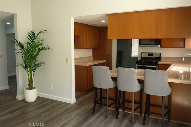 284 Celeste Dr, Riverside, CA 92507 - kitchen with stainless steel appliances, brown cabinets, a peninsula, dark wood-style floors, and a breakfast bar