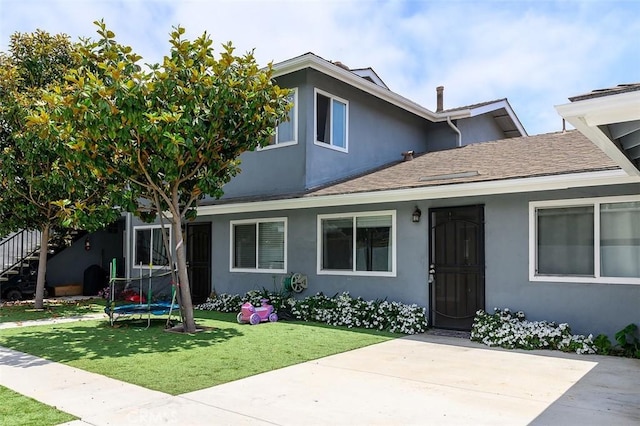17132 Emerald Ln, Huntington Beach, CA 92647 - view of front of property featuring stucco siding, a trampoline, a front yard, and a shingled roof
