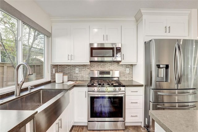 55 Fairfield, Lake Forest, CA 92610 - kitchen with appliances with stainless steel finishes, tasteful backsplash, white cabinetry, dark countertops, and light wood-type flooring