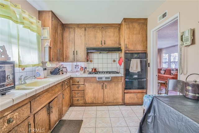 14012 S Wilkie Ave, Gardena, CA 90249 - kitchen featuring black oven, brown cabinetry, tile counters, a warming drawer, and backsplash