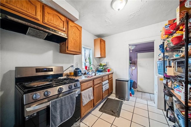 633 E 136th St, Los Angeles, CA 90059 - kitchen with stainless steel range with gas cooktop, brown cabinets, light countertops, under cabinet range hood, and light tile patterned floors