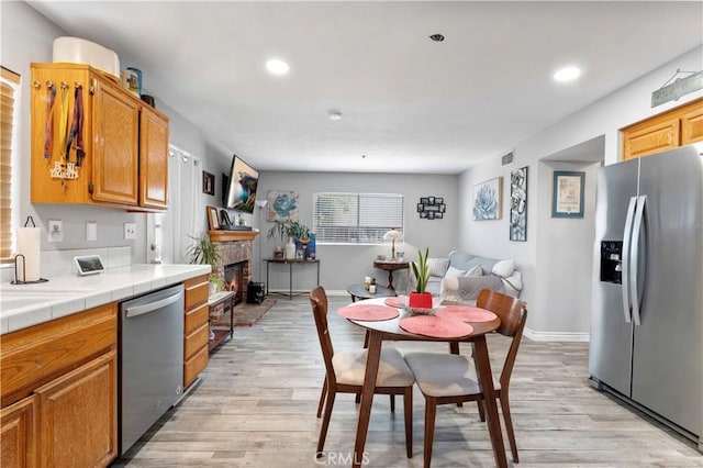 13519 Fremont St, Fontana, CA 92336 - kitchen featuring appliances with stainless steel finishes, tile counters, light wood-type flooring, recessed lighting, and a lit fireplace