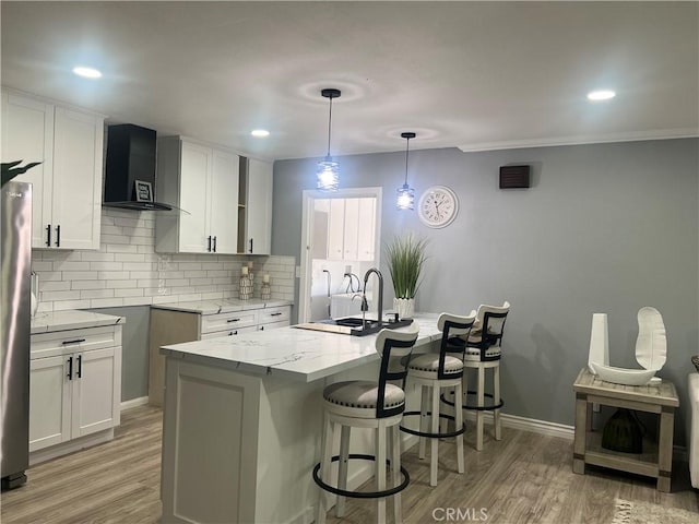 14726 Osage Rd, Apple Valley, CA 92307 - kitchen with wall chimney exhaust hood, light stone counters, a breakfast bar, light wood finished floors, and backsplash