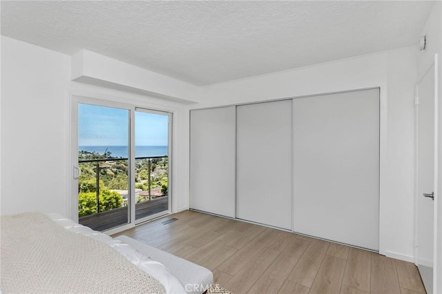 1385 Terrace Way, Laguna Beach, CA 92651 - unfurnished bedroom featuring light wood-style flooring, access to exterior, a water view, a closet, and a textured ceiling