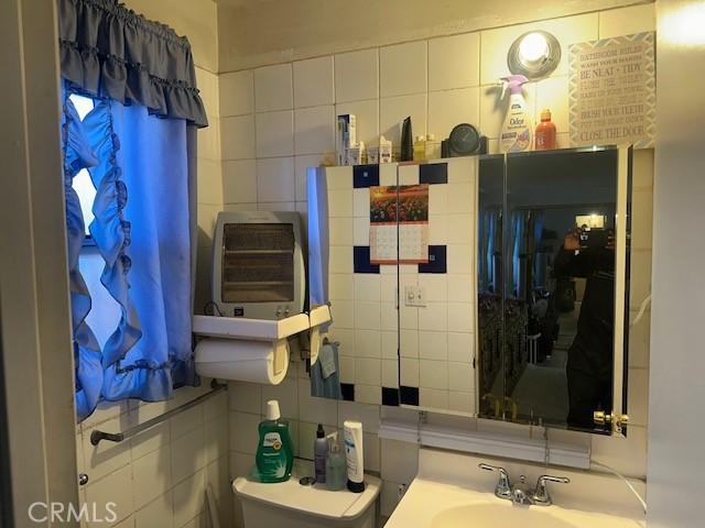 2440 Merrywood St, Pomona, CA 91767 - half bathroom featuring tile walls, toilet, a sink, and tasteful backsplash