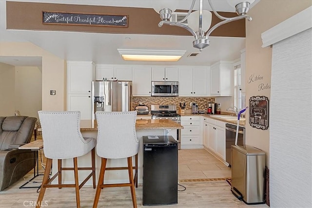 613 Flathead River St, Oxnard, CA 93036 - kitchen with appliances with stainless steel finishes, a sink, decorative backsplash, white cabinetry, and a kitchen bar