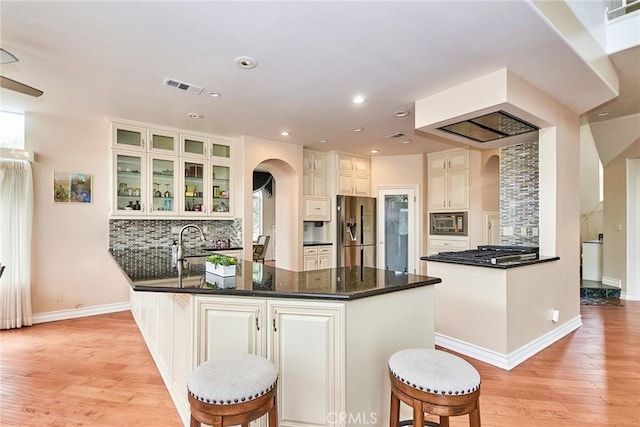 1089 Village Dr, Chino Hills, CA 91709 - kitchen featuring appliances with stainless steel finishes, a peninsula, arched walkways, light wood-style flooring, and backsplash