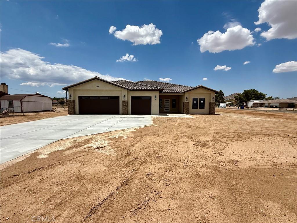 15640 Cheyenne Rd, Apple Valley, CA 92307 - view of front of home featuring a garage, driveway, a tiled roof, stone siding, and stucco siding