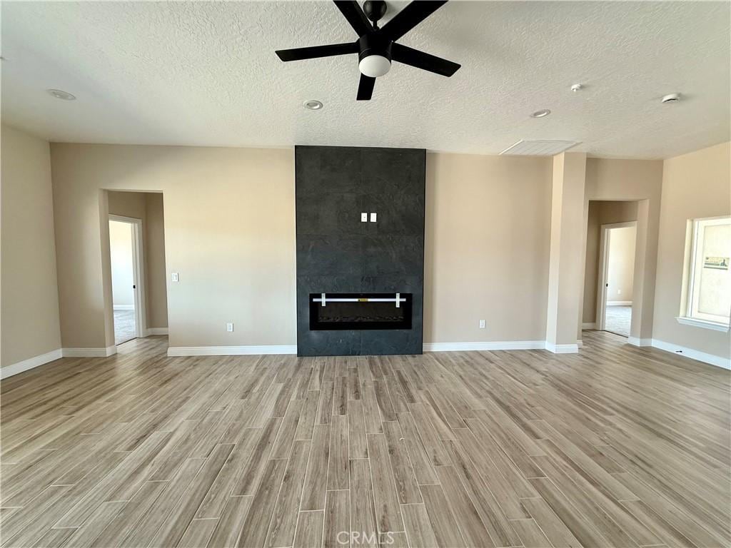 15640 Cheyenne Rd, Apple Valley, CA 92307 - unfurnished living room with light wood-type flooring, a textured ceiling, a ceiling fan, baseboards, and a tiled fireplace