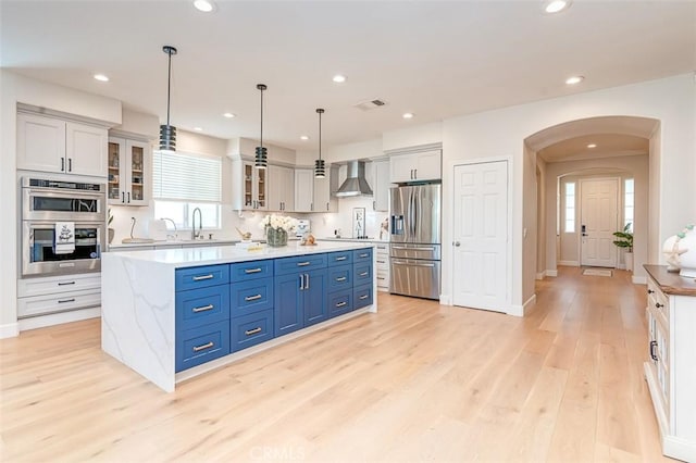 40365 Trenton Ct, Temecula, CA 92591 - kitchen with appliances with stainless steel finishes, wall chimney range hood, a kitchen island, arched walkways, and light wood finished floors