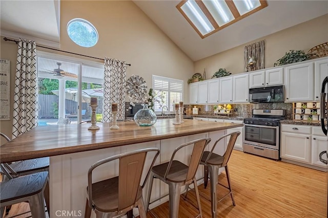 1122 Moonbeam Way, Turlock, CA 95382 - kitchen featuring stainless steel range with gas stovetop, black microwave, white cabinetry, backsplash, and high vaulted ceiling