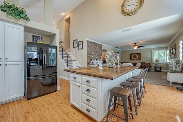1122 Moonbeam Way, Turlock, CA 95382 - kitchen with black fridge with ice dispenser, a breakfast bar area, white cabinetry, light wood finished floors, and open floor plan