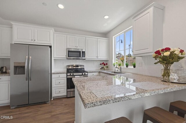 275 Fuerte Dr, Santa Paula, CA 93060 - kitchen with appliances with stainless steel finishes, a peninsula, white cabinetry, a kitchen breakfast bar, and dark wood-style floors