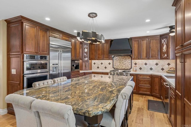 525 Hilo Way, Vista, CA 92081 - kitchen featuring stainless steel appliances, premium range hood, light wood-style flooring, a breakfast bar, and glass insert cabinets