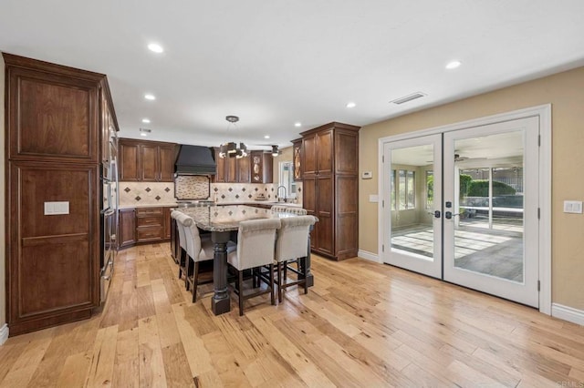 525 Hilo Way, Vista, CA 92081 - kitchen with premium range hood, light wood finished floors, french doors, tasteful backsplash, and a kitchen island