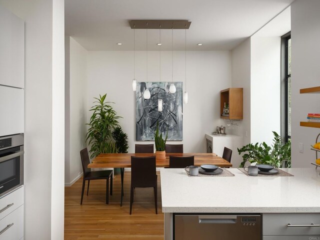 265 Coast Blvd Unit 9, La Jolla, CA 92037 - kitchen with stainless steel oven, light wood-style flooring, light stone countertops, hanging light fixtures, and healthy amount of natural light